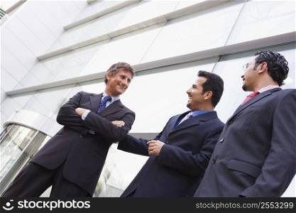 Three businessmen standing outdoors by building talking and smiling (high key/selective focus)