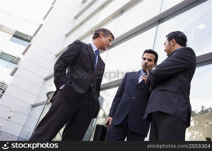 Three businessmen standing outdoors by building talking (high key/selective focus)