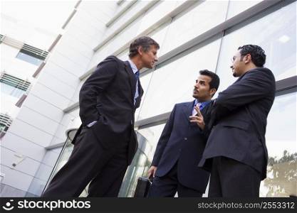 Three businessmen standing outdoors by building talking (high key/selective focus)