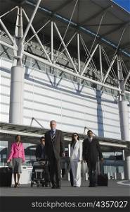 Three businessmen with two businesswomen outside at an airport
