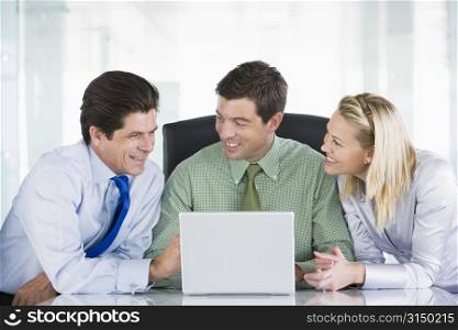 Three businesspeople in a boardroom looking at laptop smiling