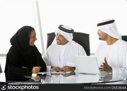 Three businesspeople in office with laptop talking and smiling (high key/selective focus)