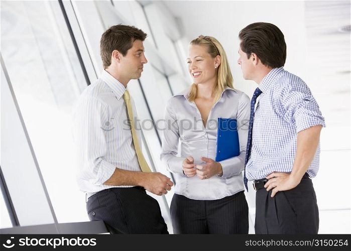 Three businesspeople standing in corridor talking and smiling