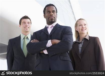Three businesspeople standing outdoors by building smiling