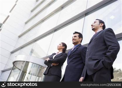 Three businesspeople standing outdoors by building smiling (high key/selective focus)