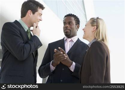 Three businesspeople standing outdoors by building talking and smiling