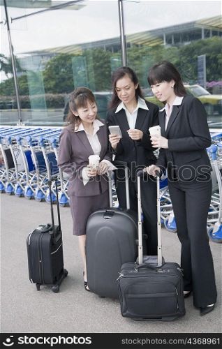 Three businesswomen looking at a personal data assistant at an airport lounge