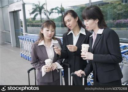 Three businesswomen looking at a personal data assistant at an airport lounge