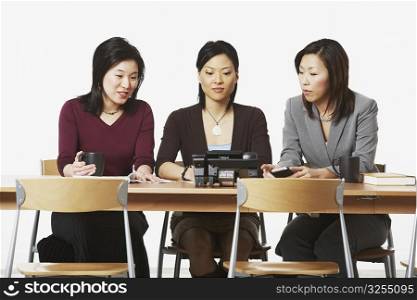 Three businesswomen sitting on chairs looking at the telephone