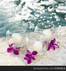 Three candles and three purple orchids by pool.