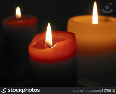 Three candles burning in the dark, focus on the front candle