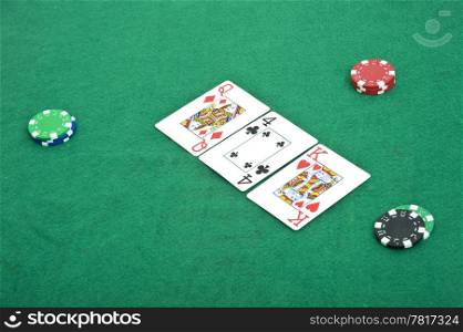 Three cards lying open on a felt covered table during the flop of a poker game, with three stacks of chips being bet
