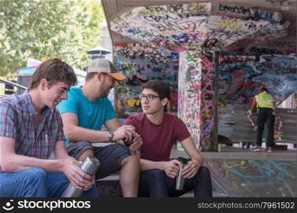 Three Casual Young Adults Drinking Coffee and Chatting in Graffiti Skate Park