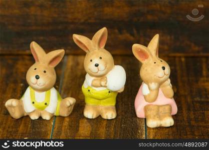 Three ceramic painted rabbits for Easter decoration on a wooden background