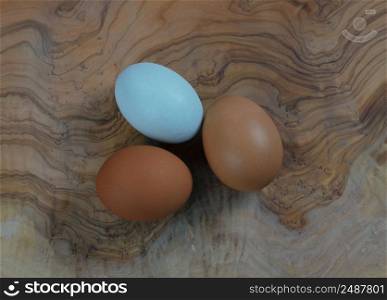 Three chicken eggs lying on natural olive wood setting in close up view 