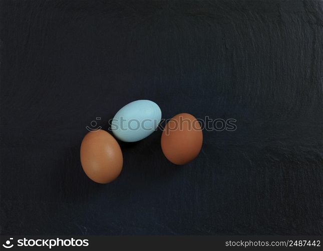 Three chicken eggs lying on natural slate stone setting