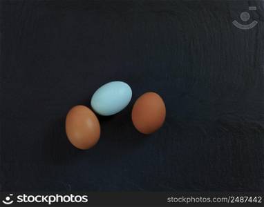 Three chicken eggs lying on natural slate stone setting