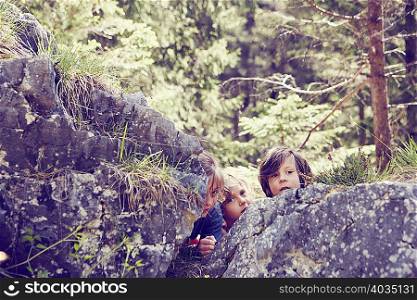 Three children hiding behind rocks in forest