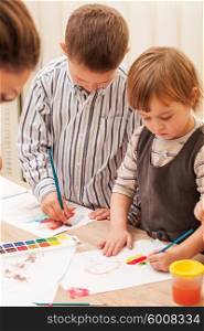 Three children learn to paint with a brush and watercolors on paper in the kindergarten. Children are painting