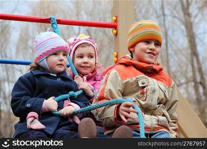 Three children on playground hold one rope