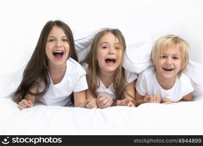 Three children waking up. Three happy smiling children waking up in bed under one blanket
