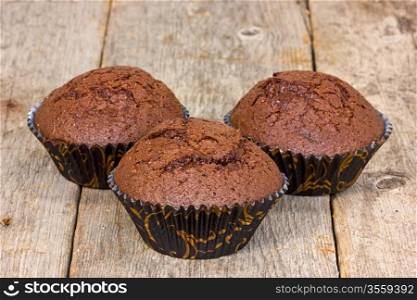 Three chocolate muffins on a wooden plank