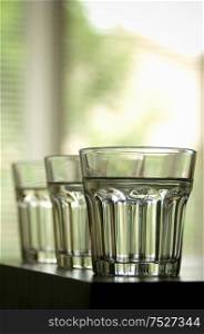 Three clear glasses lined up on a counter top.