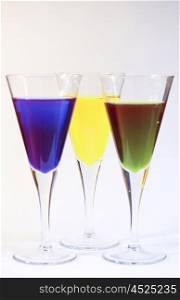 Three cocktails of bright coloured alcohol against a white background