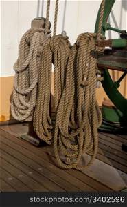 three coils of rope on a deck of sailing ship next to winch used rise sails