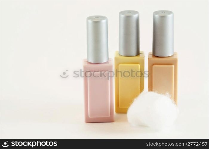 Three colored cosmetic makeup bottles in pink, beige and yellow with cotton ball isolated on white background.