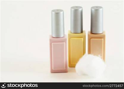 Three colored cosmetic makeup bottles in pink, beige and yellow with cotton ball isolated on white background.