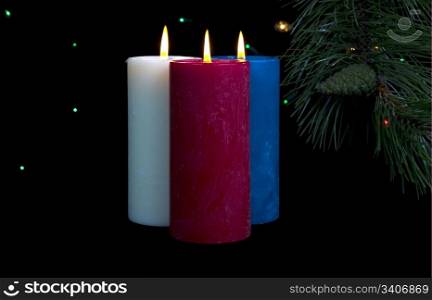 Three colorful candles burning with fir branch and cones in background