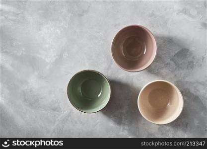 Three colorful porcelain handmade pottery bowls isolated on stone gray background with copy space, flat lay. Three colorful porcelain bowls isolated on stone gray background, flat lay