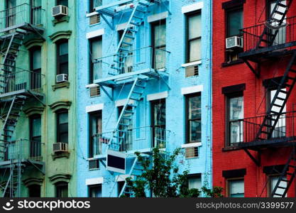 Three colorful, red, blue and green, apartment buildings facades with emergency escapes. Typical New York City, Boston or Chicago rental complexes with fire escape stairs next to the windows.