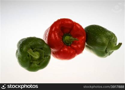Three coloured peppers with drops of water on the isolated white background.One red pepper and two green peppers.Red pepper in the middle and two green on the sides.Horizontal view.