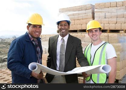 Three construction workers standing on construction site with blueprints