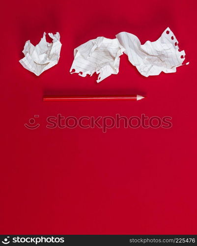 three crumpled white pieces of paper and a red wooden pencil on a red background, copy space