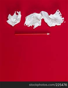 three crumpled white pieces of paper and a red wooden pencil on a red background, copy space