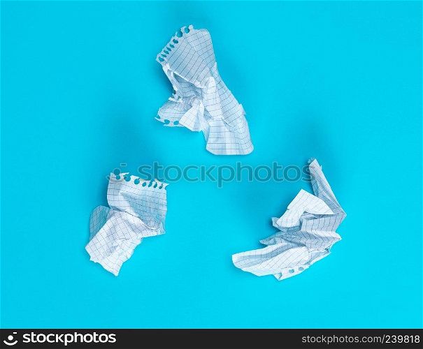 three crumpled white pieces of paper in a cell from a school notebook on a blue background
