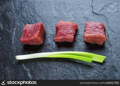 Three cubes of meat and green onions on the black stone table