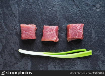 Three cubes of meat and green onions on the black stone table