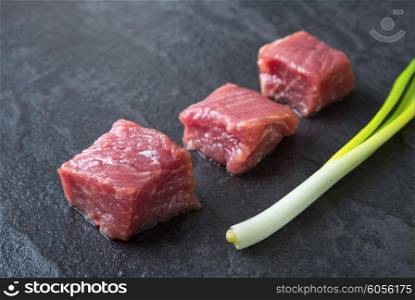 Three cubes of meat and green onions on the black stone table