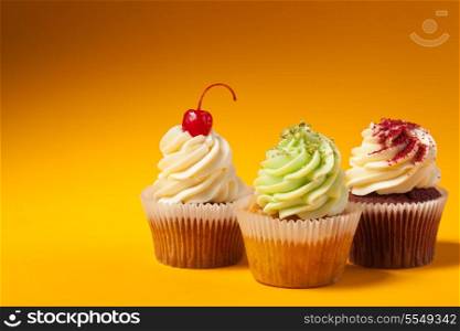 three cupcakes isolated on orange background with copyspace