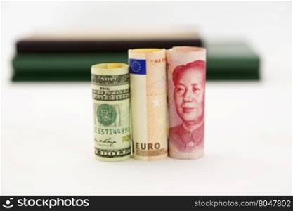 Three currencies, dollar, euro, and yen, are placed together. Selective focus on money. Books behind on white background. Financial issues of European Union, dollar, and yen are connected in global markets.