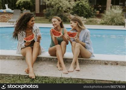 Three cute young women sitting on by the swimming pool and eating watermellon in the house backyard