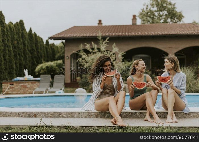 Three cute young women sitting on by the swimming pool and eating watermelon in the house backyard