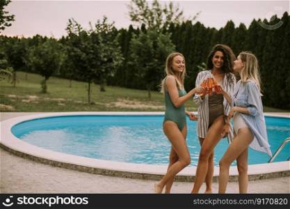 Three cute young women standing by the swimming pool and eating watermelon in the house backyard