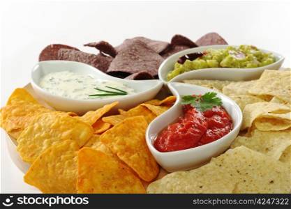 Three different dips (guacamole, tomato-chili and cream cheese dip) with salty and cheese tacos and chips made of Peruvian purple corn on white (Selective Focus) . Dips with Tacos and Chips