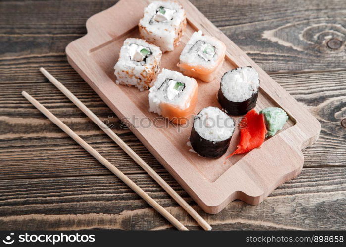 three different kinds of Japanese rolls with wasabi and ginger on bamboo tray on beautiful wooden background