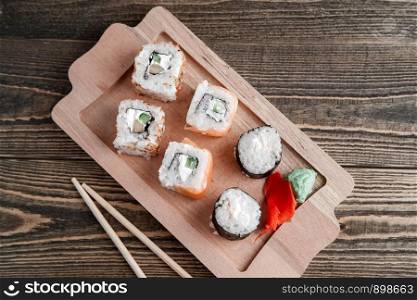 three different kinds of Japanese rolls with wasabi and ginger on bamboo tray on beautiful wooden background